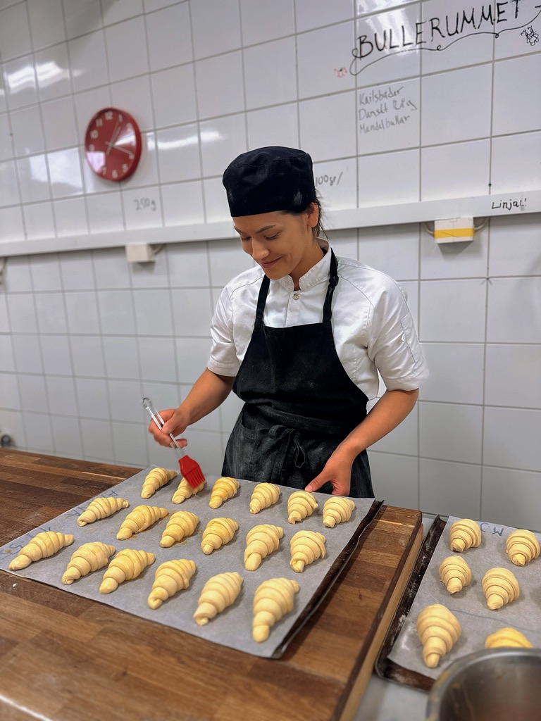 a woman in a black hat and apron making croissants